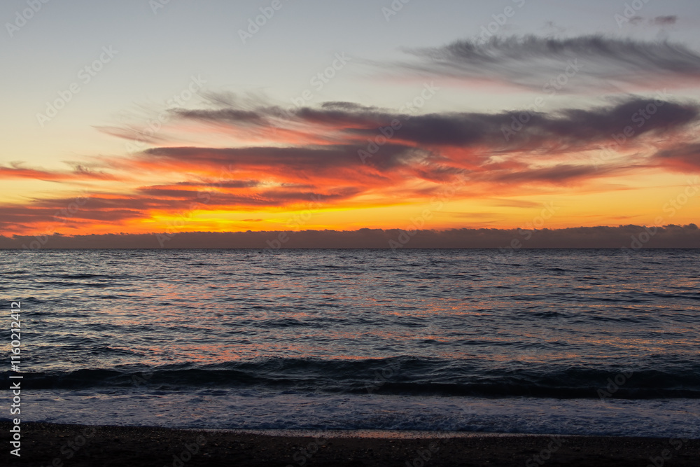 Obraz premium Orange sunset on the sea. Bright juicy landscape with feathery clouds on the horizon. Purple, lilac, pink shades of the evening sky. The smooth surface of the sea, a boat sails by. Idyll, relaxation