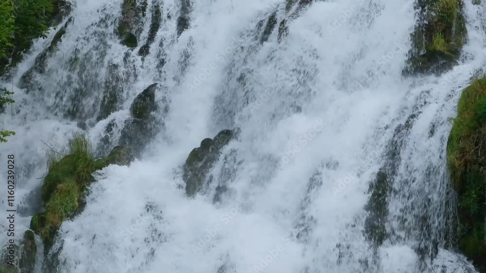 Slow-motion close-up of a waterfall. White water cascades gently over green bushes. Slow-motion close-up of a waterfall. White water cascades gently over green bushes.