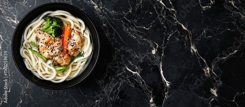 Udon noodles with vegetables and chicken in a black bowl garnished with wasabi and sesame on a black marble background photo