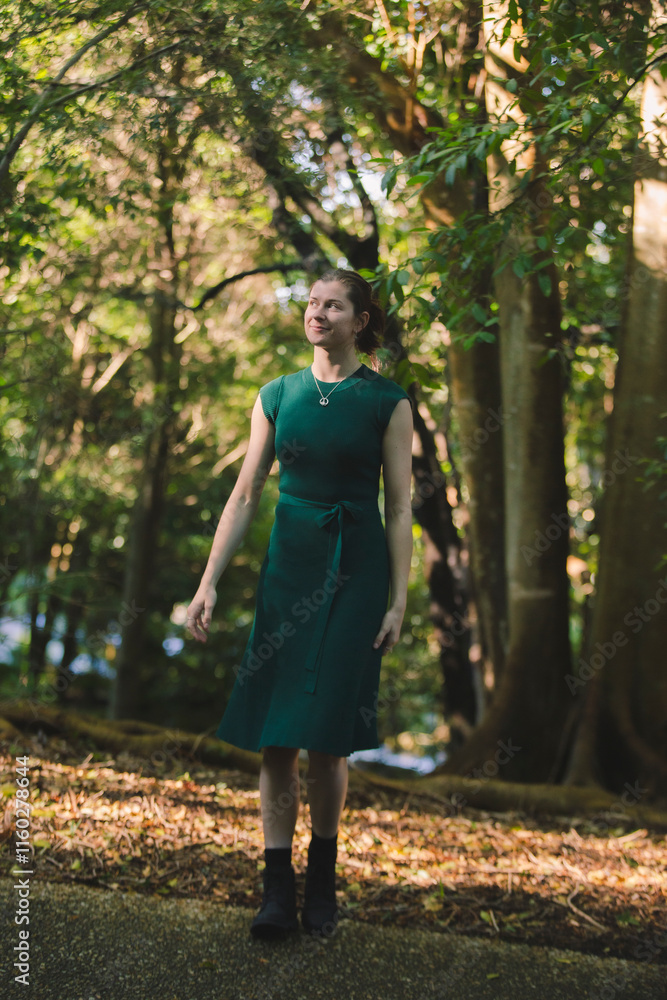 A young woman stands gracefully in a forest clearing, wearing a green dress and black boots. Sunlight filters through the dense trees, creating a serene, natural atmosphere of dappled light and shadow A young woman stands gracefully in a forest clearing, wearing a green dress and black boots. Sunlight filters through the dense trees, creating a serene, natural atmosphere of dappled light and shadow