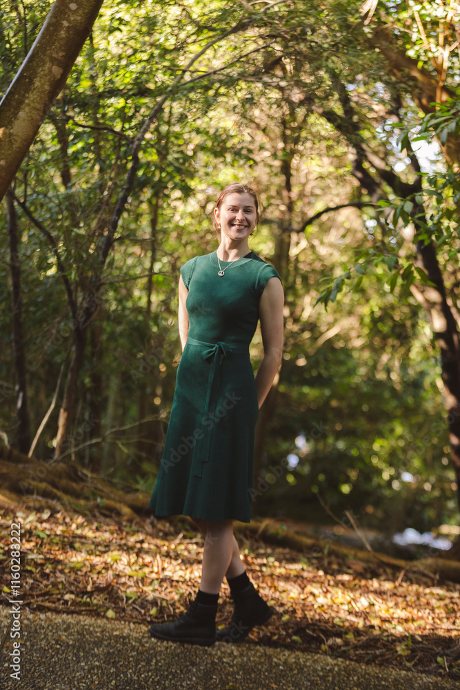 A young woman stands gracefully in a forest clearing, wearing a green dress and black boots. Sunlight filters through the dense trees, creating a serene, natural atmosphere of dappled light and shadow A young woman stands gracefully in a forest clearing, wearing a green dress and black boots. Sunlight filters through the dense trees, creating a serene, natural atmosphere of dappled light and shadow