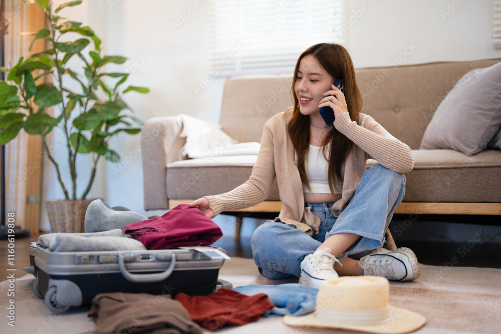 Happy young woman sitting near open suitcase with clothes, speaking on smartphone, booking travel tour, making hotel reservation or buying tickets on phone from home. Happy young woman sitting near open suitcase with clothes, speaking on smartphone, booking travel tour, making hotel reservation or buying tickets on phone from home.