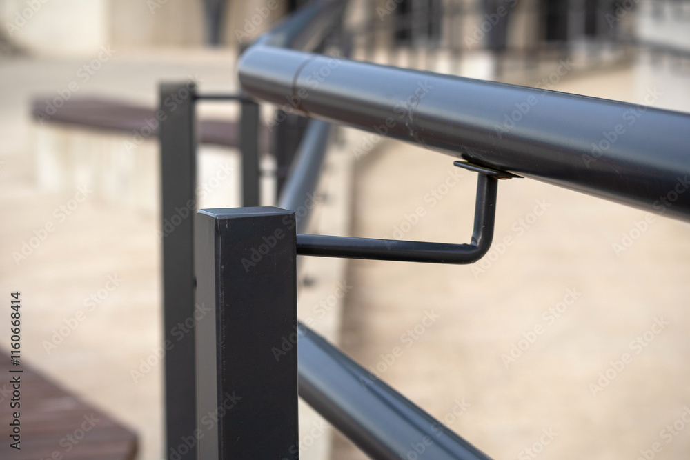 A fragment of a metal railing. The handrail consists of two parallel tubular handles attached to square metal supports. The handles and supports are painted black. A fragment of a metal railing. The handrail consists of two parallel tubular handles attached to square metal supports. The handles and supports are painted black.