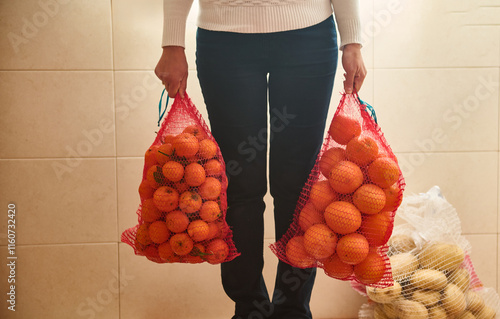 Person holding red mesh bags filled with oranges in indoor setting photo