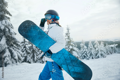 Woman Carrying Snowboard in Winter Landscape with Snow-Covered Trees.