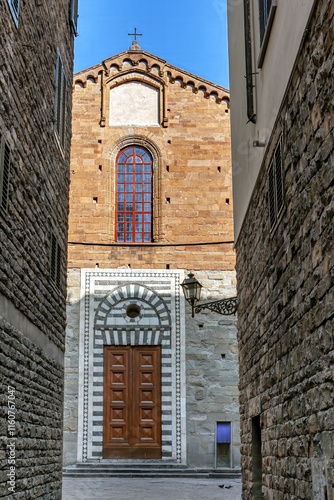 Obraz na płótnie A beautiful church with a large wooden door and intricate stonework stands between narrow alleys in Florence, Tuscany under a bright blue sky. w salonie