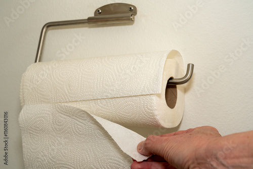 Hand is ripping off a wipe from a kitchen roll, attached to the wall. White background, white space. photo