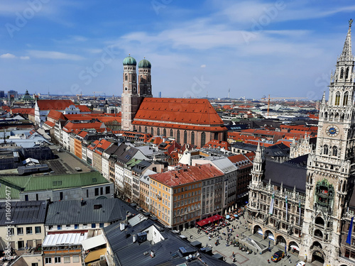 A panorama of Munich with the striking Frauenkirche and the New Town Hall on Marienplatz. Red tiled roofs characterise the old town, while the blue sky rounds off the scene. photo