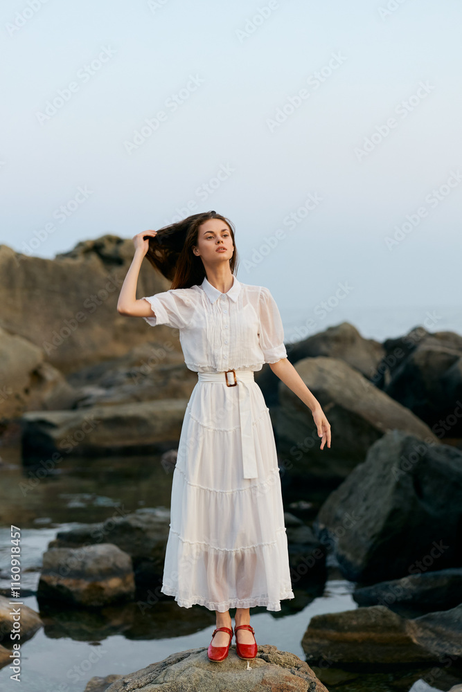 Serenity by the sea woman in white dress standing on rocky shoreline with windblown hair