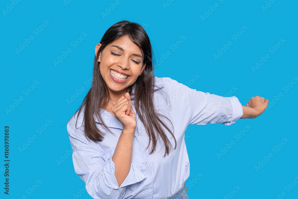 Happy woman dancing joyfully against a bright blue background while expressing delight and confidence Happy woman dancing joyfully against a bright blue background while expressing delight and confidence