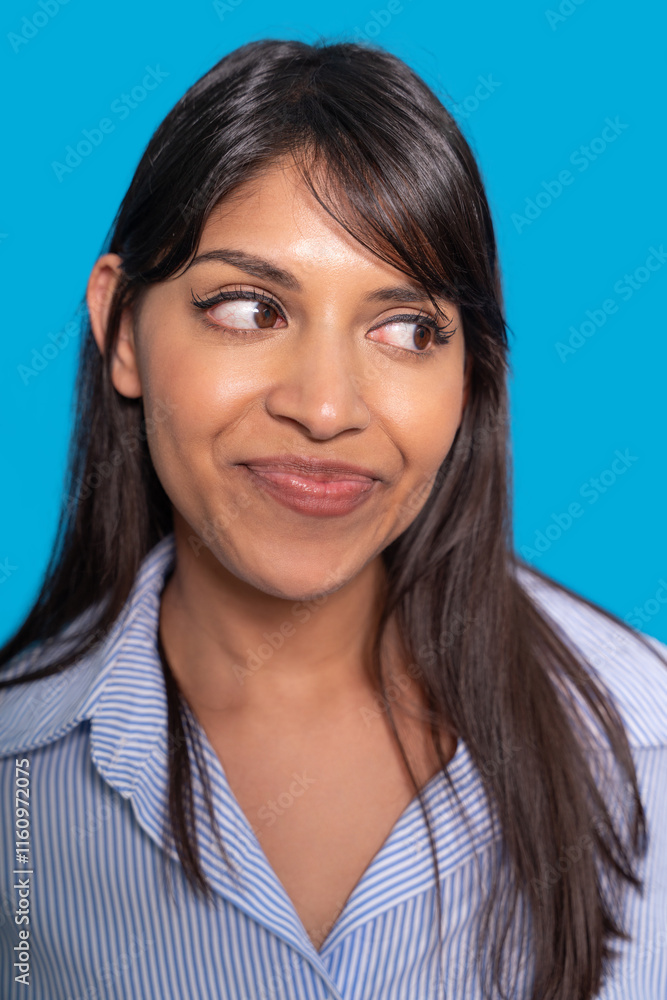Young woman with playful expression against bright blue background in casual striped shirt Young woman with playful expression against bright blue background in casual striped shirt
