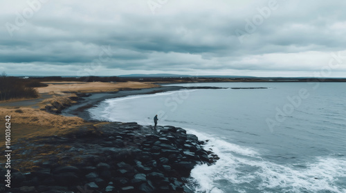 Fisherman fishing on a rocky shore in Iceland under cloudy sky