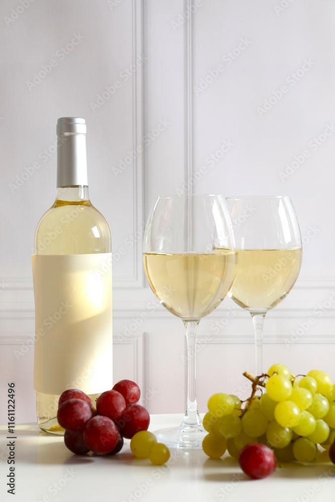 Bottle of white wine with grapes and glasses on table