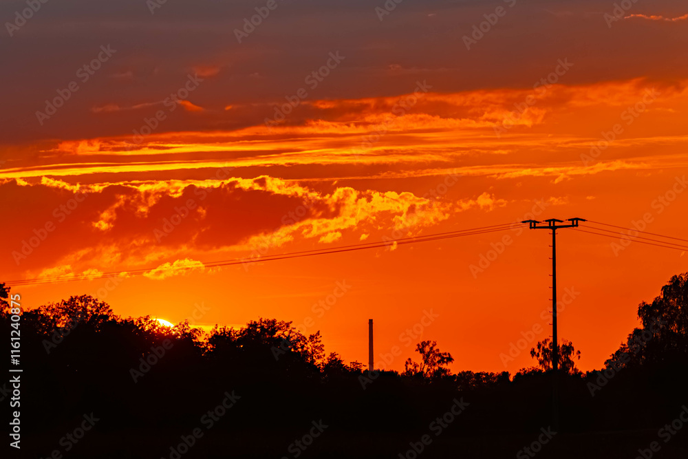 Sunset with a chimney and a powerline silhouette near Moos, Deggendorf, Bavaria, Germany Sunset with a chimney and a powerline silhouette near Moos, Deggendorf, Bavaria, Germany
