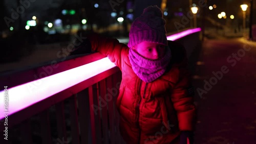 Cute little boy with Down Syndrome walking at night on a bridge lit up in glowing pink colour. 