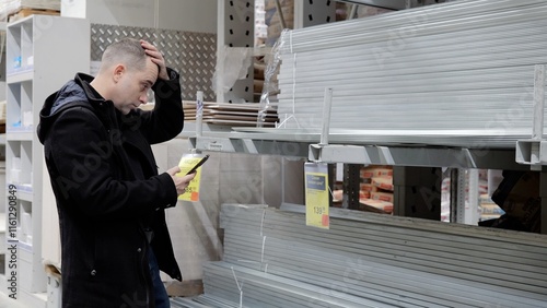Billede på lærred Confused male comparing smartphone prices with hardware store tags, contemplating purchasing construction materials with perplexed expression