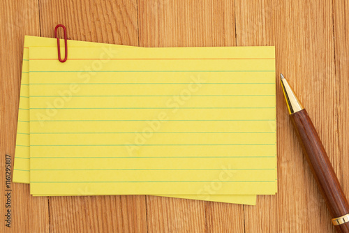 Yellow lined index cards paper with paperclip and pen on wooden desk photo