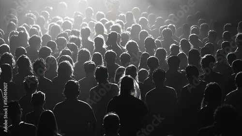 Tracking crowds gathered for a concert in silhouette backlit by stage lights. High angle shot in black and white on a telephoto lens.
