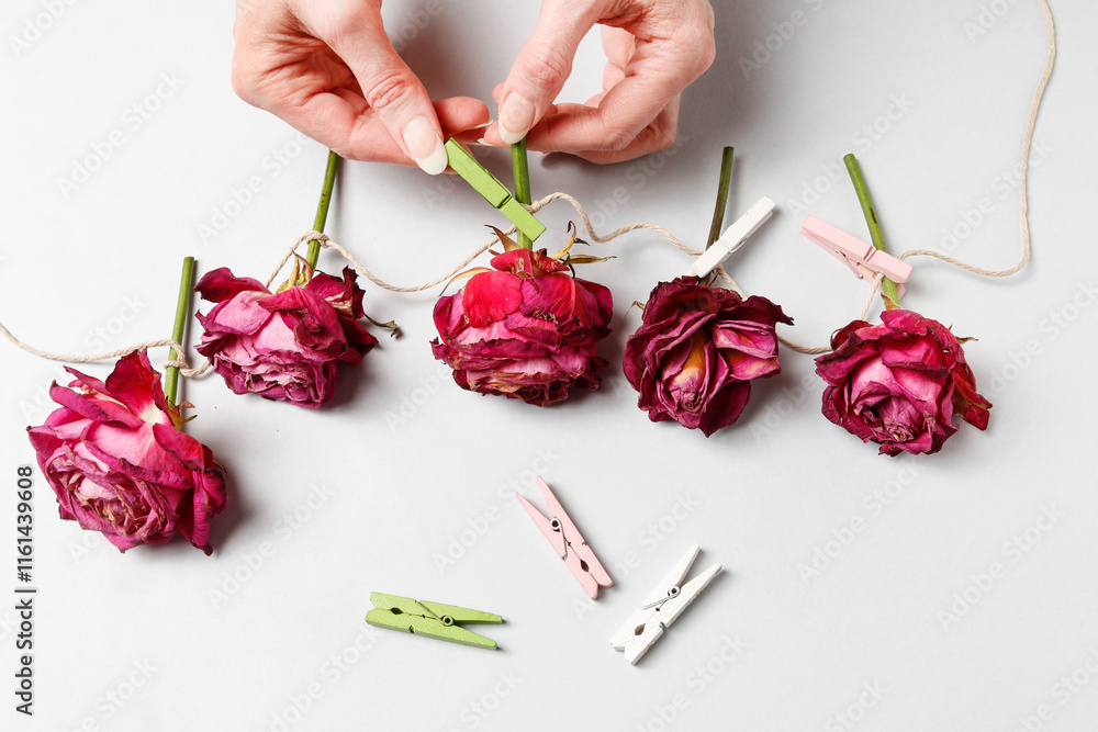 Florist at work: woman shows how to make a simple Valentine's Day decoration with semi-dry roses, string and clothes pegs. Step by step, tutorial.