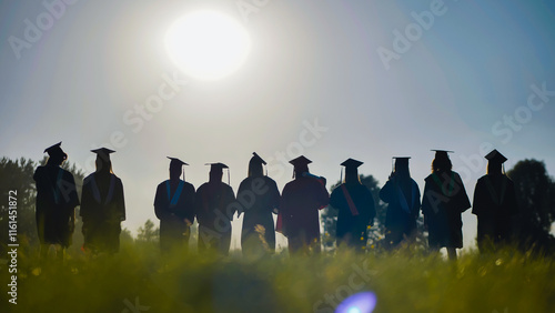 Bild auf Leinwand Graduates in cap and gown stand in a field at sunset, commemorating their high s