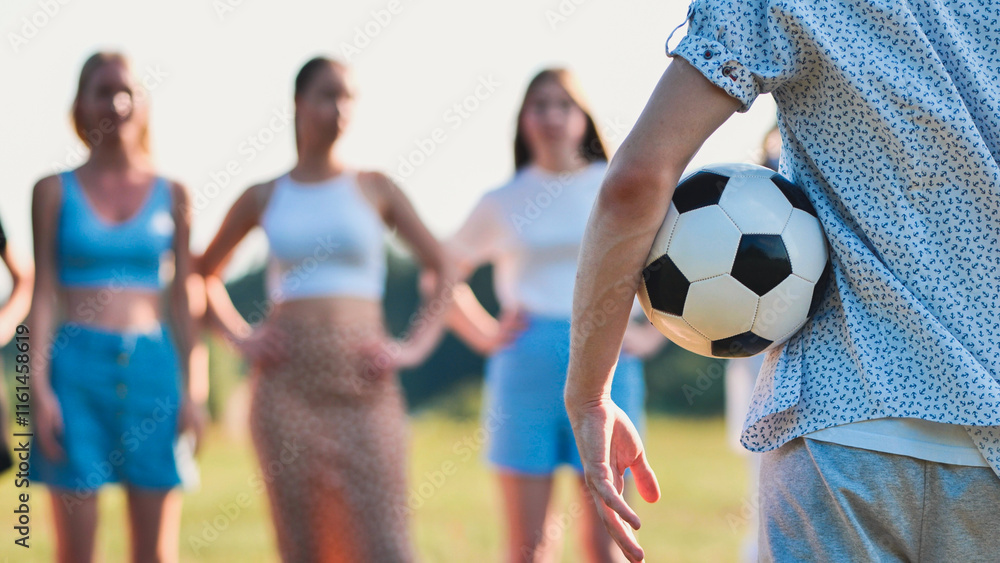Young man conceals a soccer ball behind his back as his friends wait in the background, out of focus Young man conceals a soccer ball behind his back as his friends wait in the background, out of focus