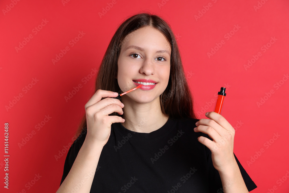 Smiling teenage girl applying lip gloss on red background Smiling teenage girl applying lip gloss on red background