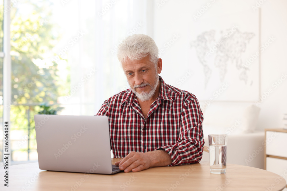 Senior man using laptop at table indoors Senior man using laptop at table indoors