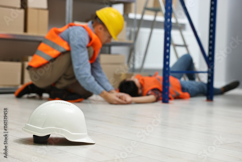 First aid. Hardhat on floor and man helping his unconscious colleague in warehouse, selective focus