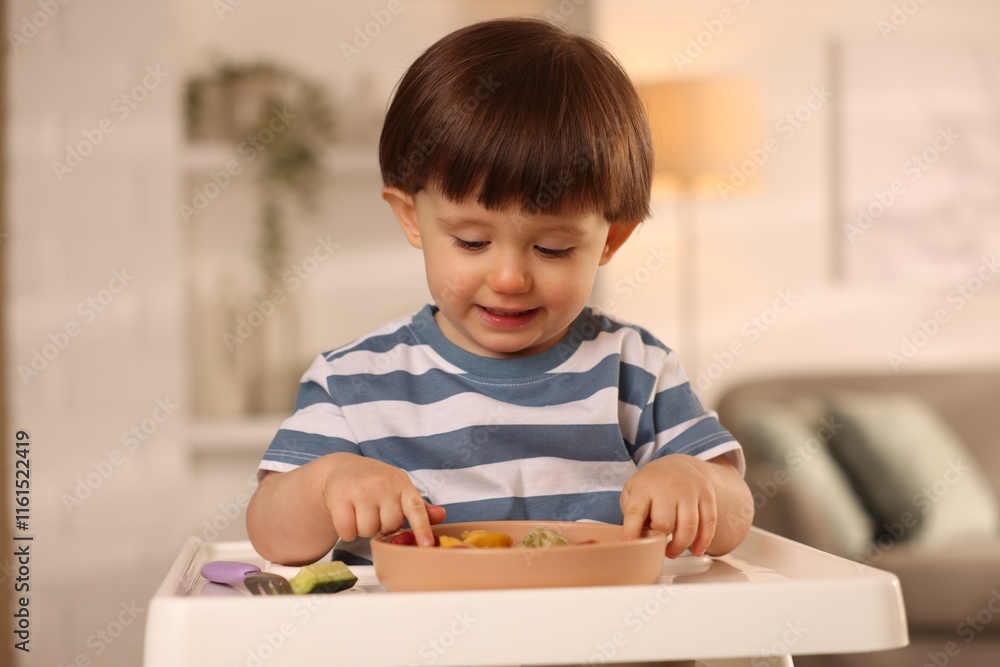 Cute little boy eating healthy food in high chair at home Cute little boy eating healthy food in high chair at home