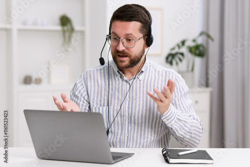 Interpreter in headset having video chat via laptop at white table indoors