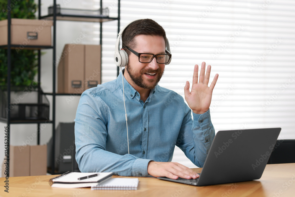 Interpreter in headphones having video chat via laptop at wooden table indoors Interpreter in headphones having video chat via laptop at wooden table indoors
