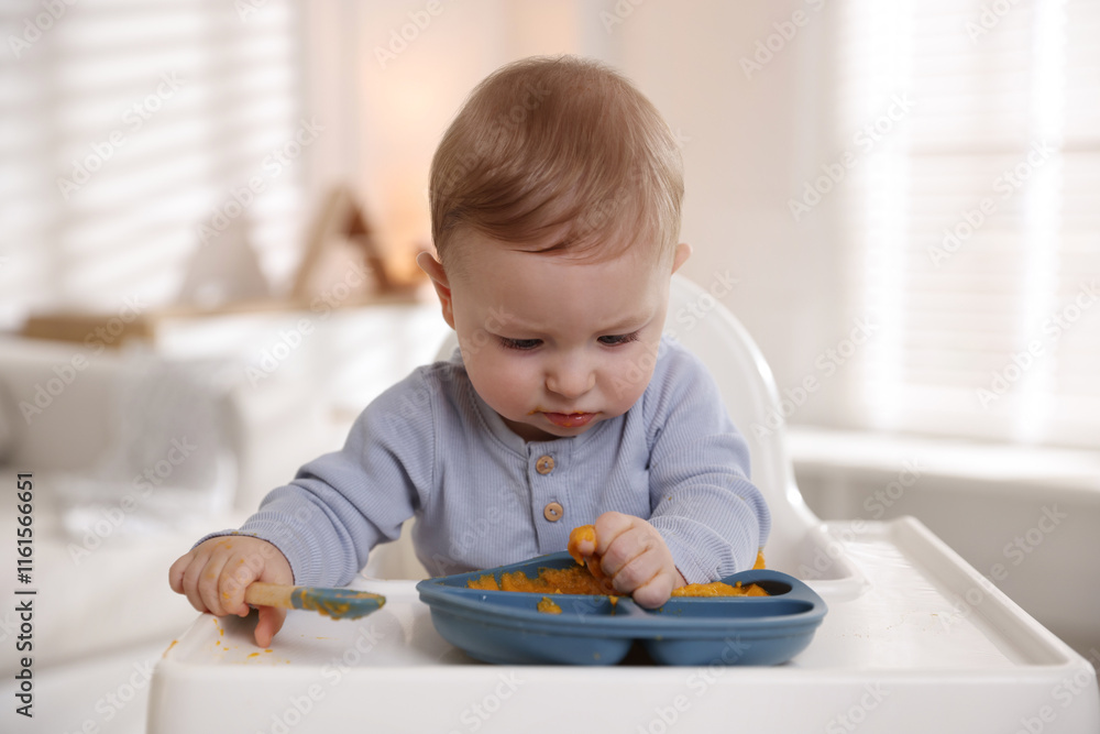 Cute little baby eating healthy food in high chair indoors Cute little baby eating healthy food in high chair indoors