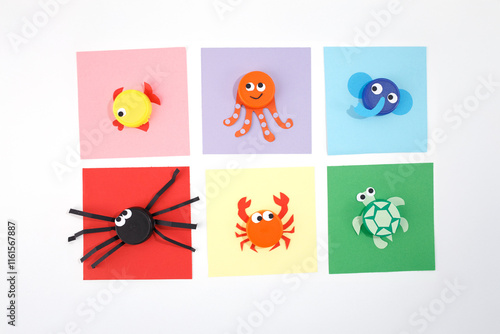 plastic bottle caps transformed into different samples of animals on color square paper. Minimalist flat lay composition on white background. DIY children summer activity and recycling concept. photo