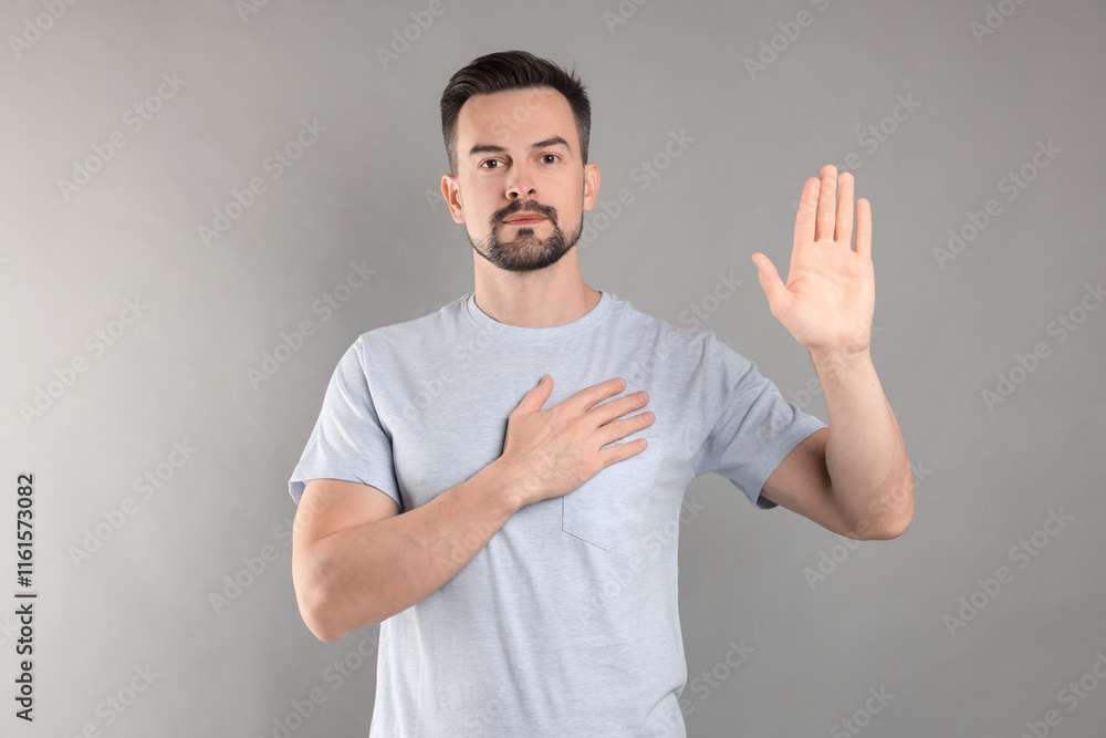 Man making promise with raised hand on grey background. Oath gesture Man making promise with raised hand on grey background. Oath gesture