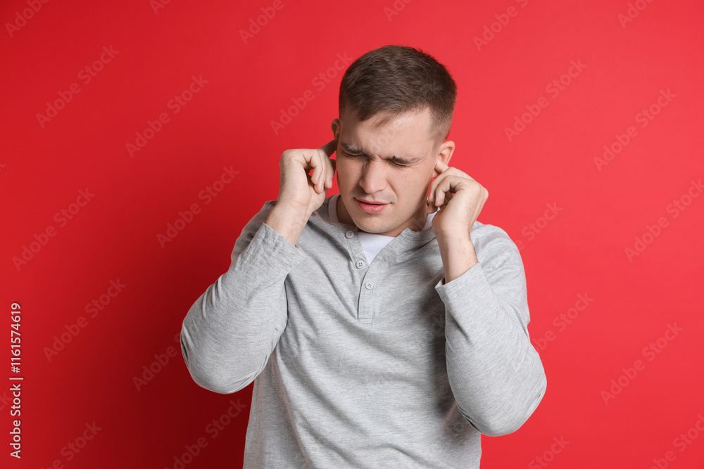 Man covering his ears with fingers on red background Man covering his ears with fingers on red background