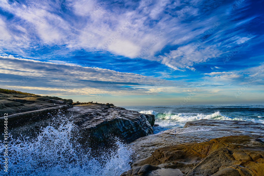 Obraz premium 2023-12-31 THE ROCKY SHORELINE IN LA JOLLA CALIFORNIA WITH WAVES HITTING THE ROCKS SPLASHING WITH A NICE INTENSE SKY NEAR SAN DIEGO CALIFORNIA