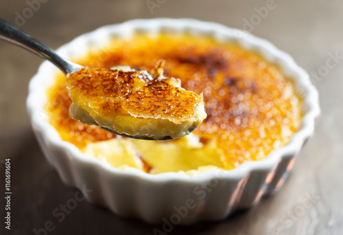 Crème brûleé spoon. crème brûleé in a white bowl with a wooden bottom.