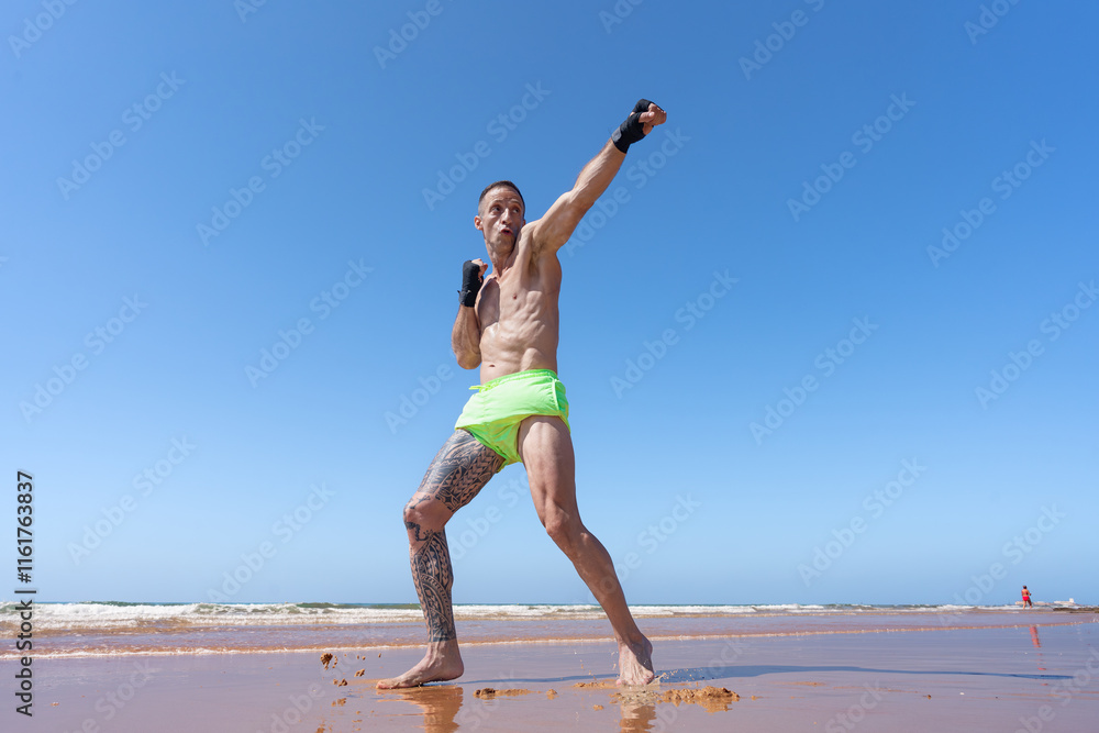Obraz premium Hombre luchador de kick boxing dando un puñetazo, un día soleado con cielo azul de verano en la playa haciendo deporte.