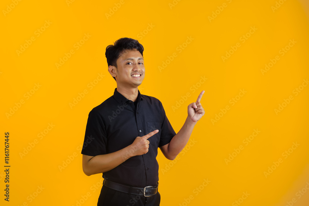 A happy young student points to the side with fingers on a yellow background A happy young student points to the side with fingers on a yellow background