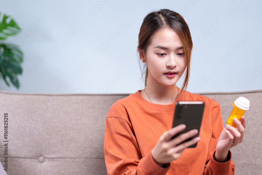 A young woman sitting on a sofa, carefully reading medication information on her phone while holding a pill bottle A young woman sitting on a sofa, carefully reading medication information on her phone while holding a pill bottle
