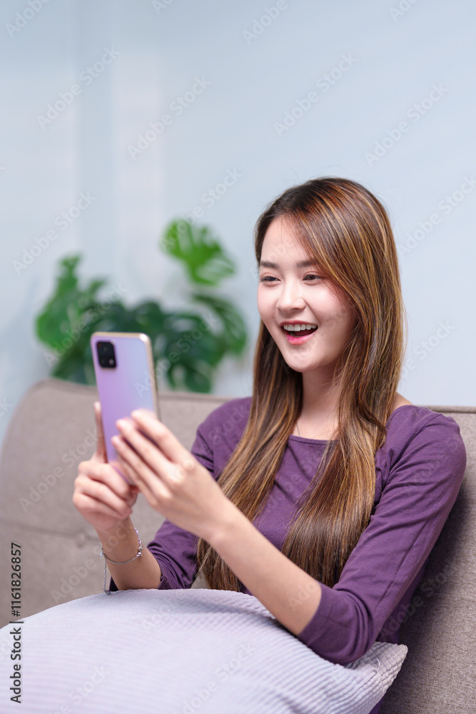 A young woman video calling on her smartphone while sitting on a sofa, engaging in a lively conversation A young woman video calling on her smartphone while sitting on a sofa, engaging in a lively conversation