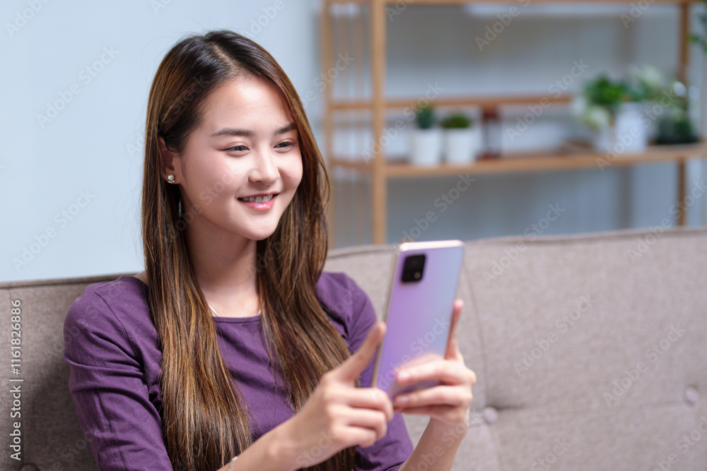 A young woman video calling on her smartphone while sitting on a sofa, engaging in a lively conversation A young woman video calling on her smartphone while sitting on a sofa, engaging in a lively conversation