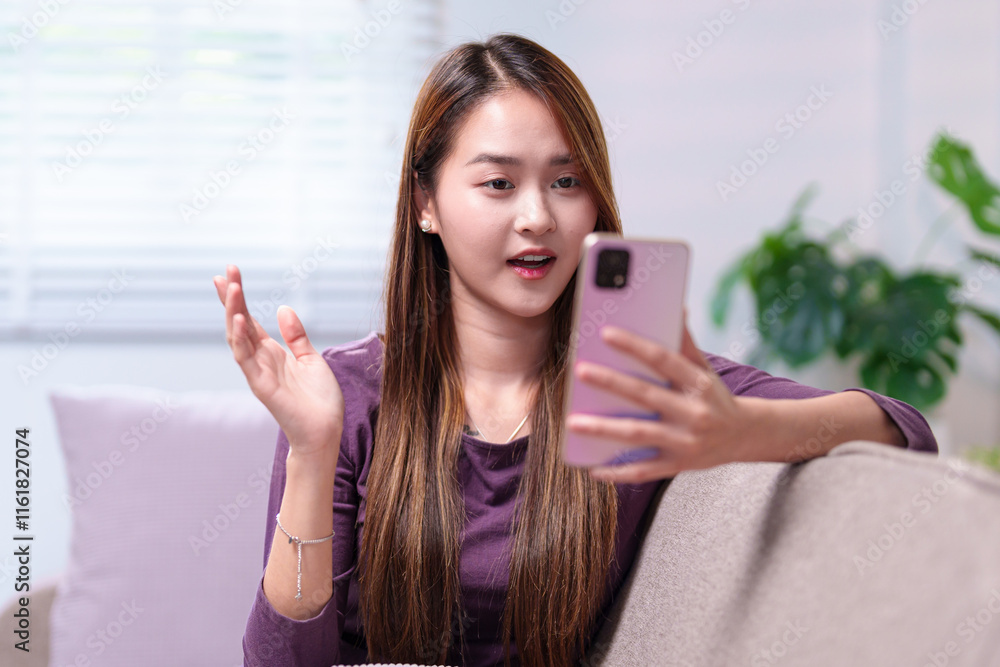 A young woman video calling on her smartphone while sitting on a sofa, engaging in a lively conversation A young woman video calling on her smartphone while sitting on a sofa, engaging in a lively conversation