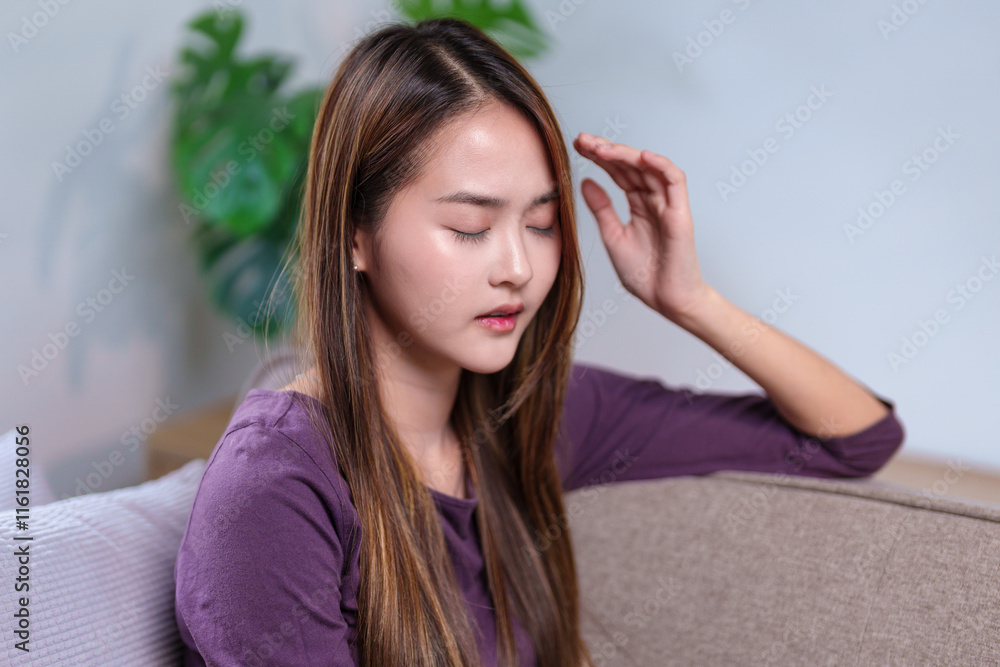 A woman resting her hand on her head, appearing to be in a thoughtful or reflective moment while sitting on a sofa A woman resting her hand on her head, appearing to be in a thoughtful or reflective moment while sitting on a sofa