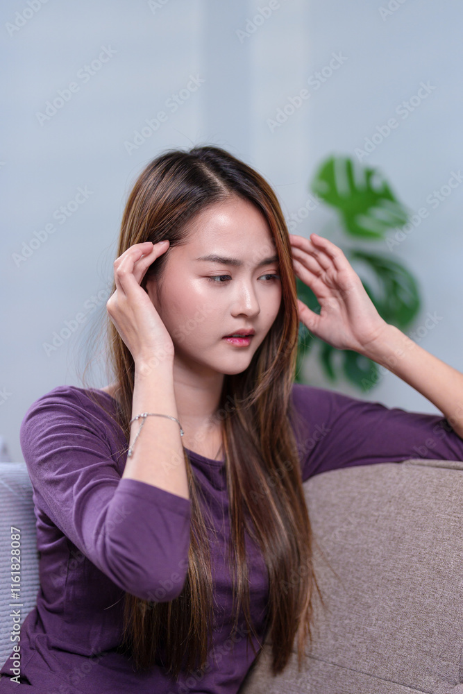 Obraz premium A woman resting her hand on her head, appearing to be in a thoughtful or reflective moment while sitting on a sofa