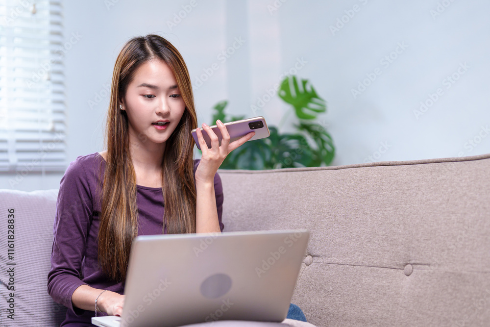 A young woman multitasking by speaking on a phone while working on her laptop, sitting in a relaxed home environment. A young woman multitasking by speaking on a phone while working on her laptop, sitting in a relaxed home environment.