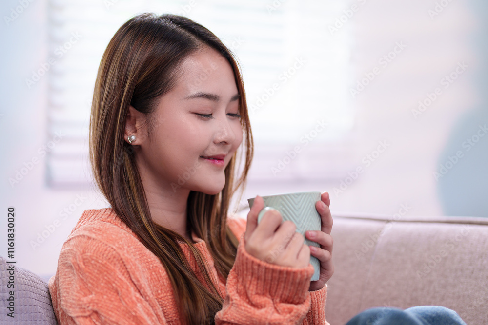 A young woman seated comfortably, holding a mug of coffee close, smiling softly, dressed in a cozy orange sweater, enjoying a peaceful moment. A young woman seated comfortably, holding a mug of coffee close, smiling softly, dressed in a cozy orange sweater, enjoying a peaceful moment.