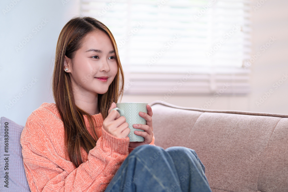 A young woman seated comfortably, holding a mug of coffee close, smiling softly, dressed in a cozy orange sweater, enjoying a peaceful moment. A young woman seated comfortably, holding a mug of coffee close, smiling softly, dressed in a cozy orange sweater, enjoying a peaceful moment.