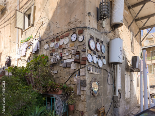 Art installation featuring clock plaques with inscriptions and other crafts on corner of old building in old part of Ako city in Israel photo