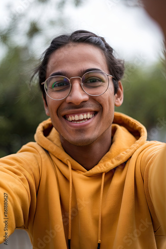 Cheerful young Indian man in yellow hoodie taking a selfie, POV shot